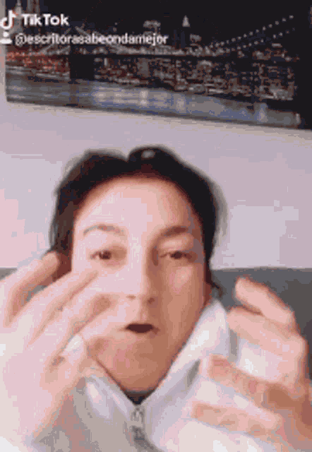 a woman is making a funny face with her hands in front of a picture of new york city .