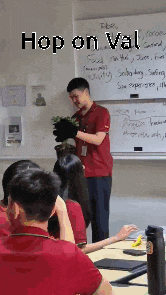 a man in a red shirt is giving a presentation in front of a white board with the words hop on val written on it