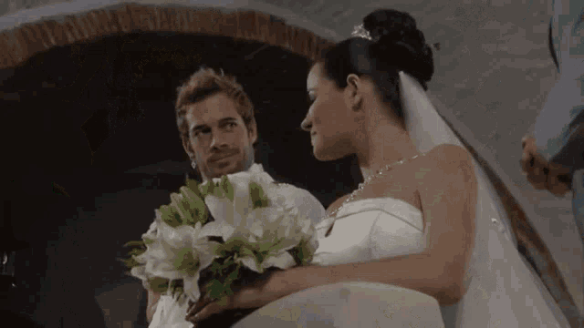 a bride and groom are standing next to each other and the bride is holding a bouquet of white flowers