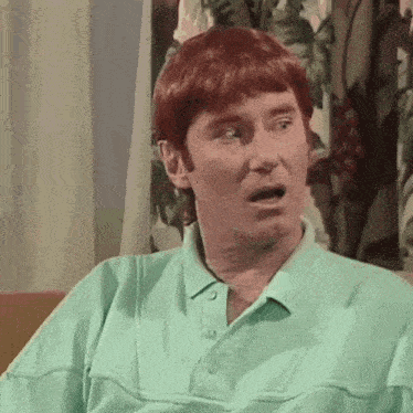 a man with red hair and a green shirt is sitting on a couch .