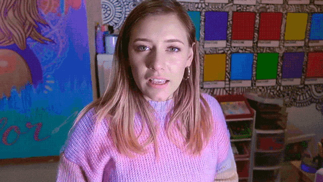 a woman wearing a purple sweater stands in front of a wall with pantone colors