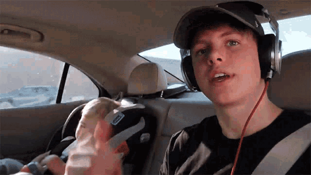a young man wearing headphones is sitting in a car with a baby in a car seat