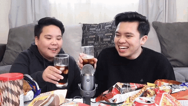 two men toasting with drinks in front of a microphone in front of a pillow that says shanghai