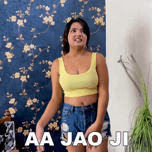 a woman in a yellow tank top and blue shorts is standing in front of a wall that says aa jao ji