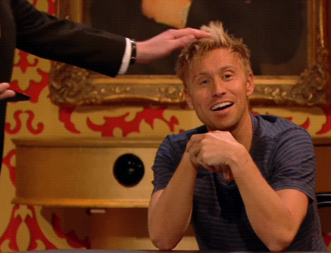 a man is sitting at a table with his hands folded and a man is putting his hand on his hair .