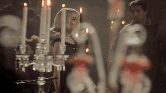 a woman in a black dress stands in front of a candle chandelier