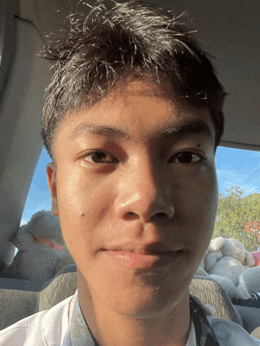 a young man sitting in a car with stuffed animals in the back seat