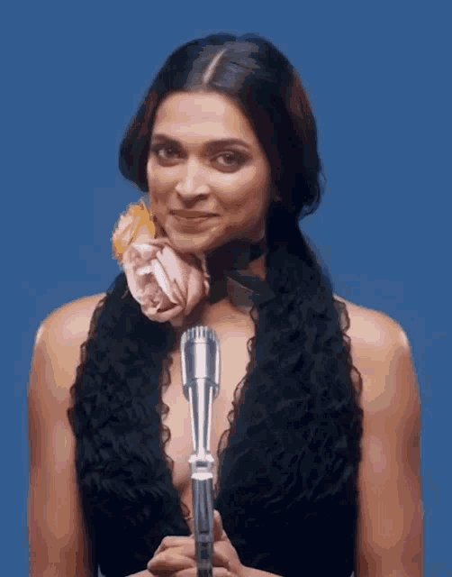 a woman in a black dress is holding a microphone and a flower