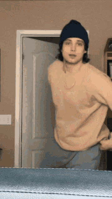 a young man wearing a beanie and a tan sweater is standing in front of a door