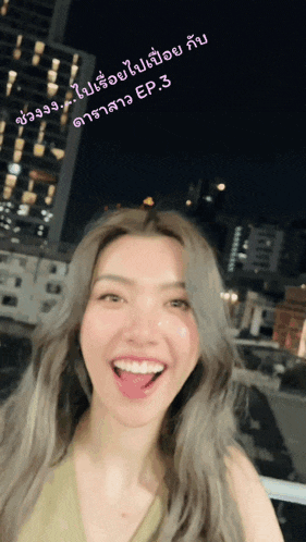 a woman in a green top is smiling in front of a city skyline at night