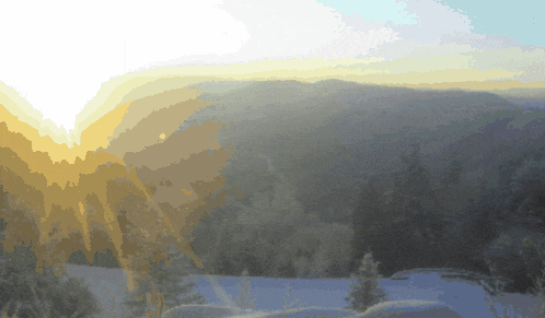 the sun is shining through the clouds over a snowy forest