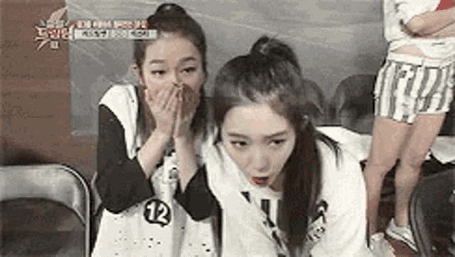 two girls are sitting next to each other and covering their mouths .