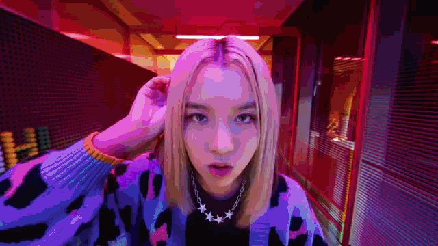 a woman with blonde hair is wearing a purple cardigan and a necklace with stars .