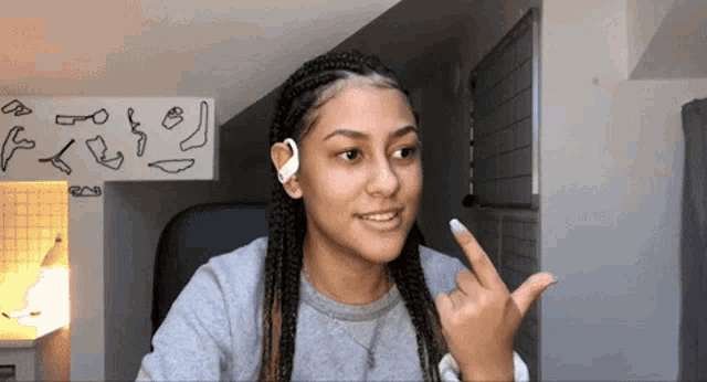a girl with braids giving the middle finger in front of a wall with drawings on it