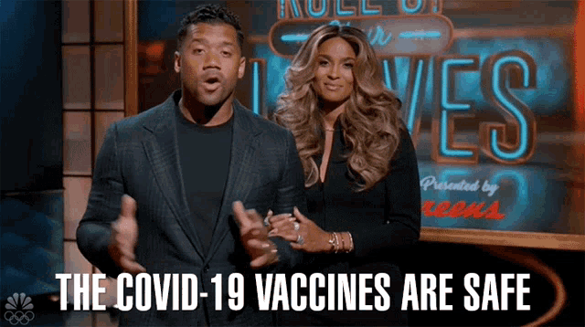 a man and a woman are standing in front of a sign that says " the covid-19 vaccines are safe "
