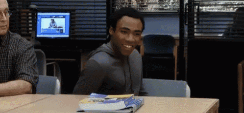 a man is smiling while sitting at a desk with books on it .