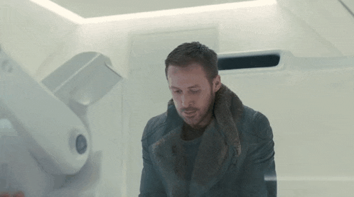 a man in a fur coat is standing in a room with a white wall .