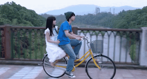 a man and a woman are riding a bicycle on a bridge over a body of water .