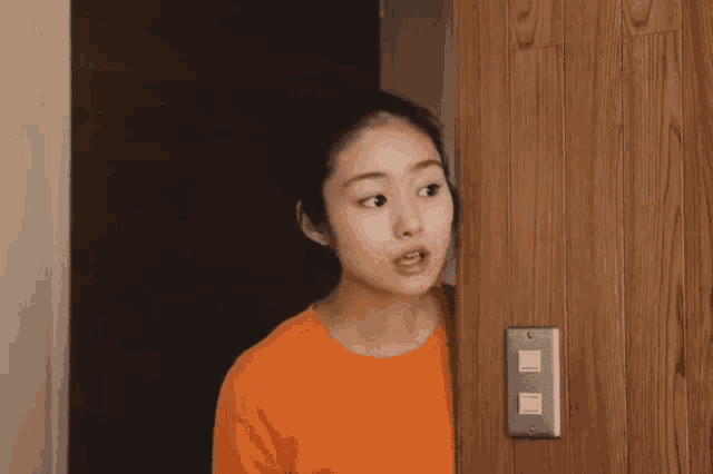 a woman in an orange sweater is standing in front of a wooden door