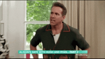 a man in a green shirt is standing in front of a window with his hands on his hips in a room .