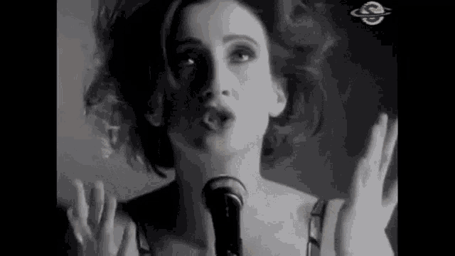 a woman is singing into a microphone with her hands in the air .