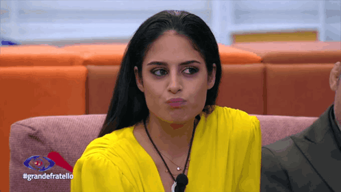a woman in a yellow top is sitting on a pink couch with the words grandefratello on the bottom