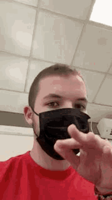 a man wearing a red shirt and a black face mask is making a peace sign .