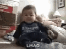 a baby is sitting on a bed with a blanket and a stack of boxes .