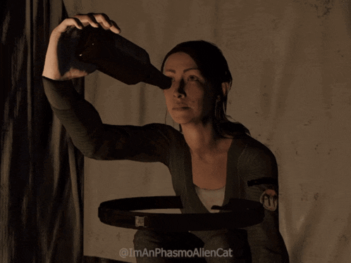 a woman is holding a bottle in front of her face and the caption says i'm an phasmoaliencat