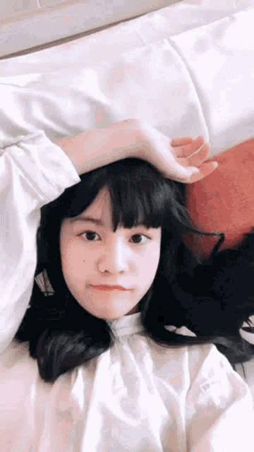 a girl with black hair is laying on a bed with her hand on her head
