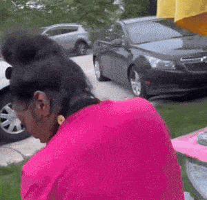 a woman in a pink shirt is standing in front of a car