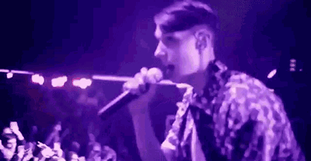 a man is singing into a microphone on a stage in front of a crowd of people .
