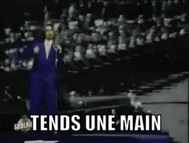 a man in a blue suit stands in front of a crowd with the words tends une main below him