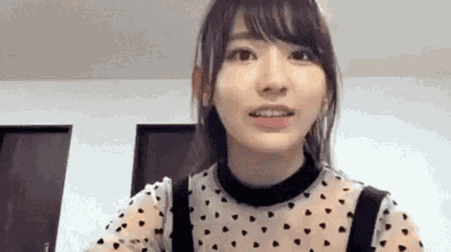a young woman wearing a polka dot shirt and suspenders is looking at the camera and smiling .