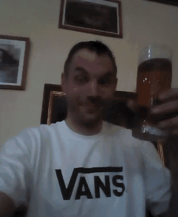 a man wearing a vans t-shirt holds a glass of beer