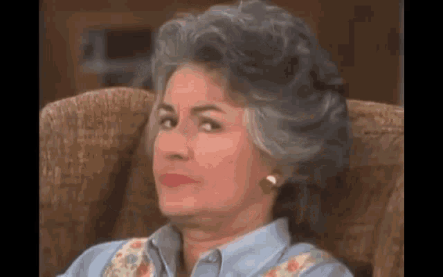 an older woman with gray hair is sitting in a chair making a funny face .