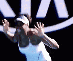 a woman in a white tank top and hat is playing tennis in front of a kia logo .