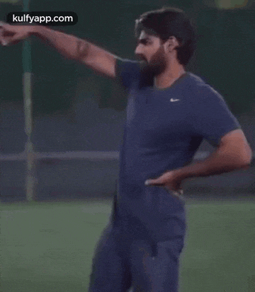 a man in a blue shirt and blue pants is standing on a field with his hands on his hips .