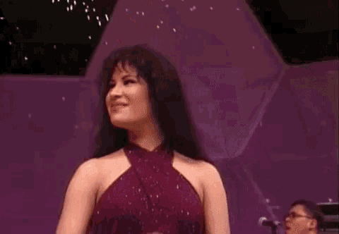 a woman in a purple dress is smiling on a stage while a man plays a piano in the background .