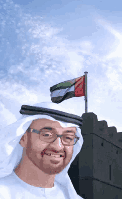 a man wearing glasses stands in front of a flag and a castle