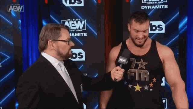 two men are standing in front of a wall that says aew wrestling dynamite