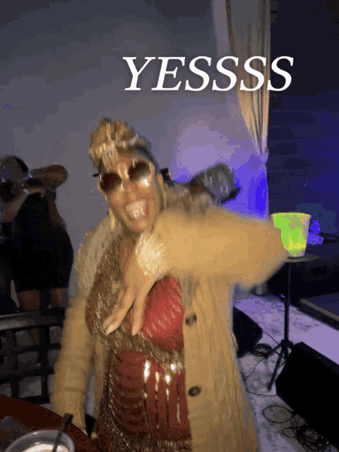 a woman wearing sunglasses and a crown stands in front of a sign that says yesss