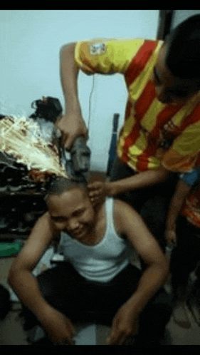 a man in a yellow and red striped shirt is cutting a man 's hair