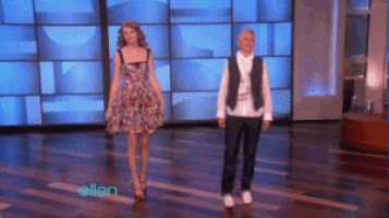 a woman in a floral dress stands next to a man in a vest on a stage with the word ellen on the bottom right