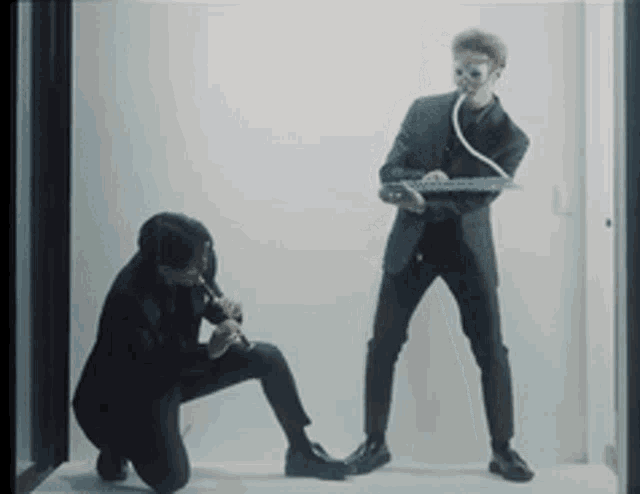 a man in a suit is playing a flute while another man in a suit is holding a keyboard