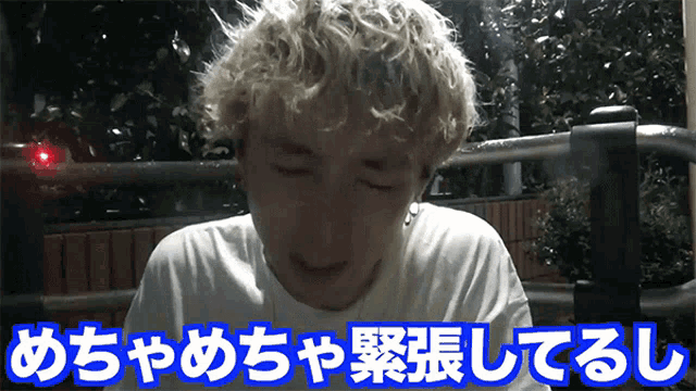a man with blonde curly hair is wearing a white t-shirt with blue writing on it