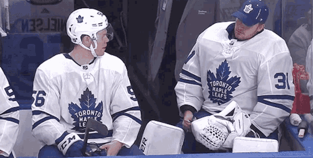 two toronto maple leafs hockey players sitting on the bench