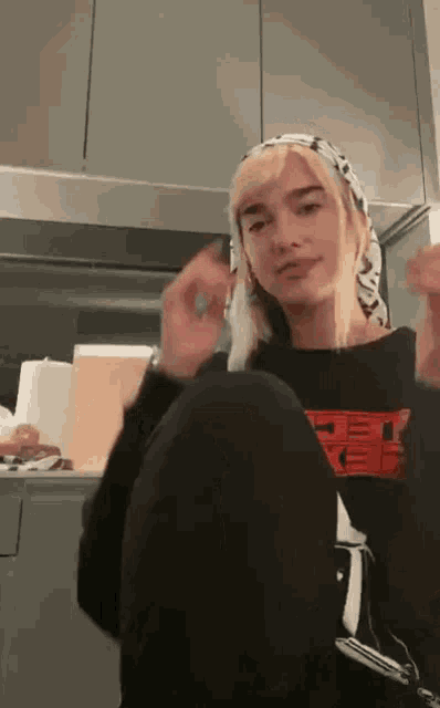 a woman with blonde hair wearing a head scarf and a black shirt that says ' off white ' on it .