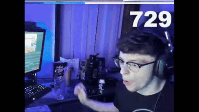 a man wearing headphones and glasses is sitting in front of a computer with the number 729 on the screen
