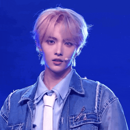 a young man wearing a denim jacket and tie stands in front of a microphone